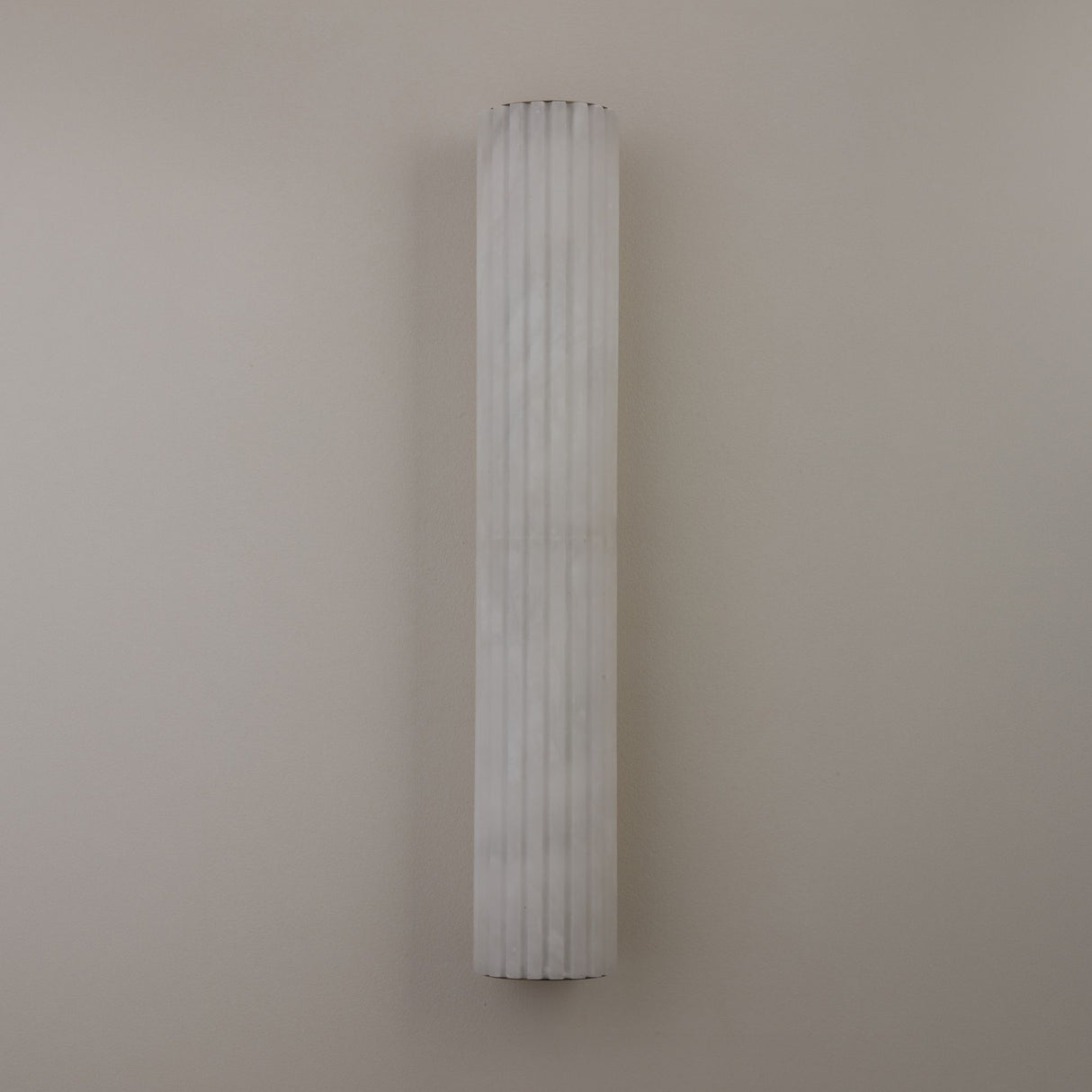 Niori Zenvia LED wall light with a tall fluted natural alabaster column in soft white, mounted vertically against a plain neutral wall.