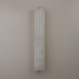 Niori Zenvia LED wall light with a tall fluted natural alabaster column in soft white, mounted vertically against a plain neutral wall.