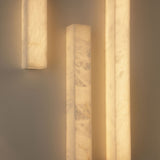 Niori Aureline LED alabaster column wall lights mounted vertically, showing warm-lit Spanish alabaster sleeves with natural veining against a neutral wall.