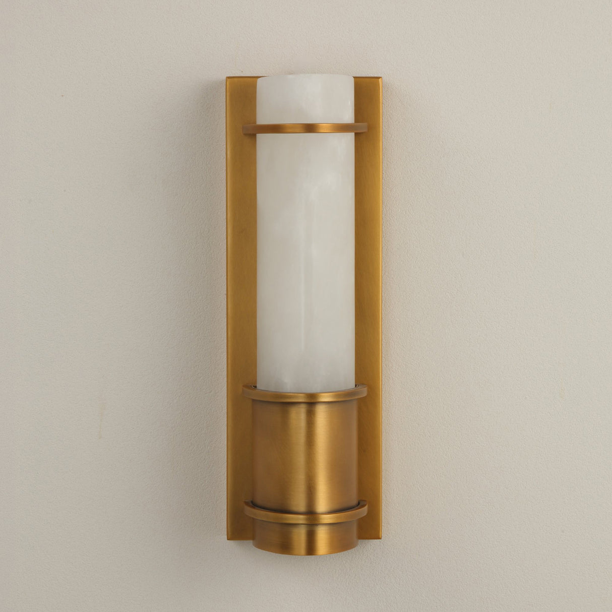 Niori Averna Small LED wall light with a Spanish alabaster cylinder framed by brushed brass bands and backplate, mounted on a pale wall.