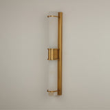 Niori Averna LED framed wall light with two stacked natural alabaster cylinders held in a brushed brass frame and central collar, mounted on a pale wall.