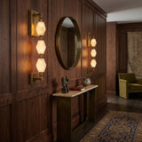 Brisalda 3 Light Faceted Alabaster Wall Light in brushed brass, mounted in pairs beside a round mirror in a wood-panelled hallway.