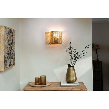 Noko Small Rattan Wall Light in natural woven cane, half-drum shape, mounted in a hallway above a wooden console table with candle holders and a vase.