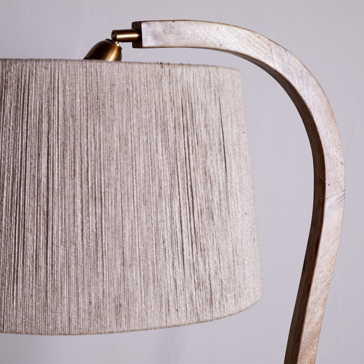Close-up of the Namira Mango Wood Floor Lamp Base's curved arm and brass lampholder fitting above a woven natural fabric shade, against a plain light background.