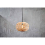Noko Large Wicker Round Pendant Light in natural woven wicker, flattened globe shape with ribbed segments, hung on black flex against a plain grey wall, bulb glowing inside.