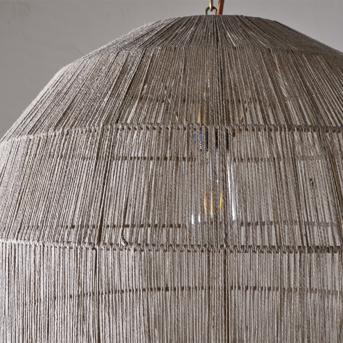 Close-up of the Nilaveli Woven Jute Sphere Pendant Light in natural tones, showing dense vertical thread winding over a visible frame with a glowing bulb inside.
