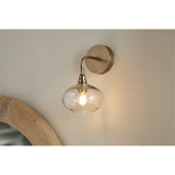Otoro Recycled Glass Wall Light in Clear, shown on a neutral wall with brass round plate, curved arm, ribbed collar and flattened clear glass shade exposing a lit bulb.