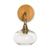 Otoro Recycled Glass Wall Light in Clear, featuring a round brass wall plate, curved brass arm, and flattened glass shade on a ribbed brass collar revealing the bulb.