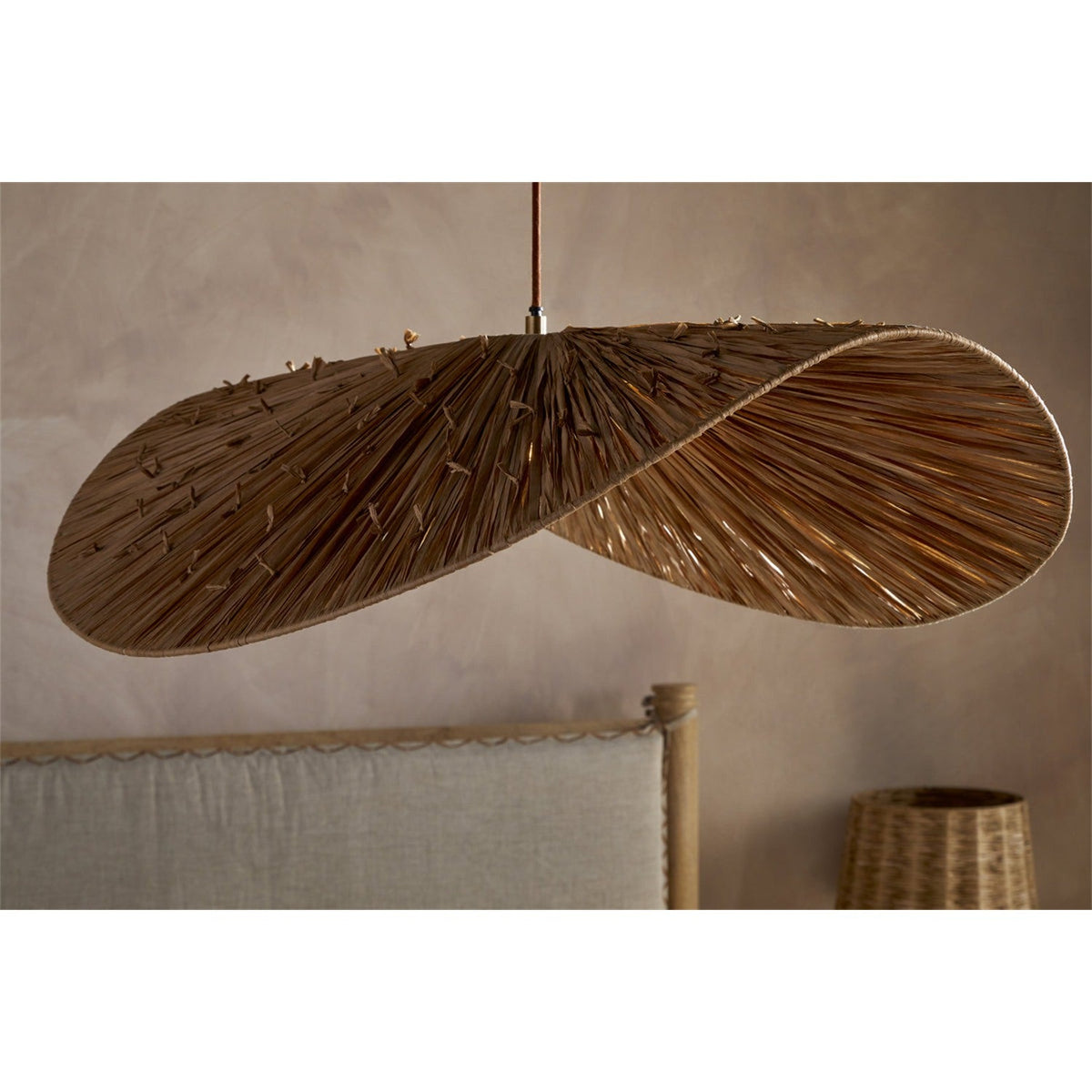 Essubi Raffia Organic Weave Pendant Light in natural tones, shown as a folded leaf-shaped shade with radiating strands and knotted detailing, hung above a bedroom headboard.