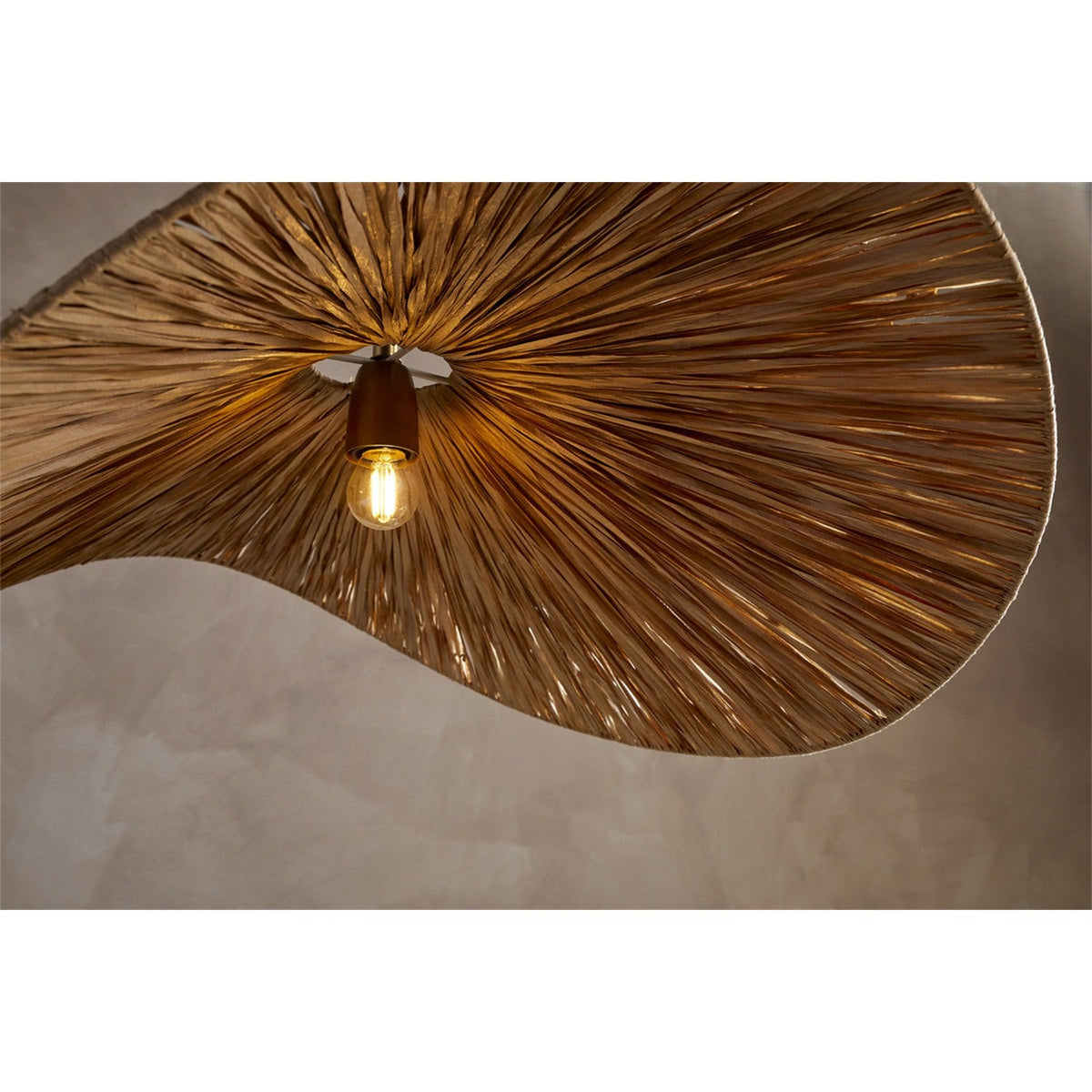Close-up of the Essubi Raffia Organic Weave Pendant Light in natural tones, showing radiating raffia strands, a curled leaf-shaped fold, and a single exposed bulb at the centre.