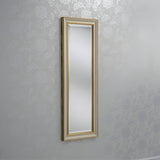 The Napoli Rectangle Wall Mirror in gold and ivory is mounted on a patterned wall. The subtle floral designs in light gray offer an elegant decor backdrop, exuding the charm of luxurious home decor.