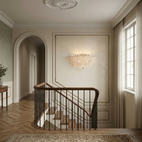 Elegant staircase with wooden handrail and black balusters in a softly lit hallway featuring light walls, a large window, crystal wall sconce, decorative ceiling molding, patterned rug, and the Amara 4 Light K9 Crystal Flush Ceiling Light in chrome.