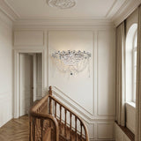 Elegant stairway with a wooden handrail and parquet floor, featuring ornate wall molding, the Amara 5 Light K9 Crystal Flush Ceiling Light in chrome, and tall arched windows with beige curtains letting in natural light.