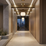 Niori Yoyo G9 Glass Pendant Lights in gold hang in a wood-panelled hallway with stone floor, planter of grasses, and city skyline view at dusk.
