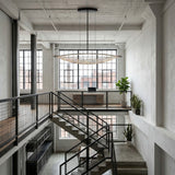 Niori Amara LED K9 crystal chandelier in chrome, a long leaf-shaped fitting suspended in an industrial loft interior with tall factory windows.