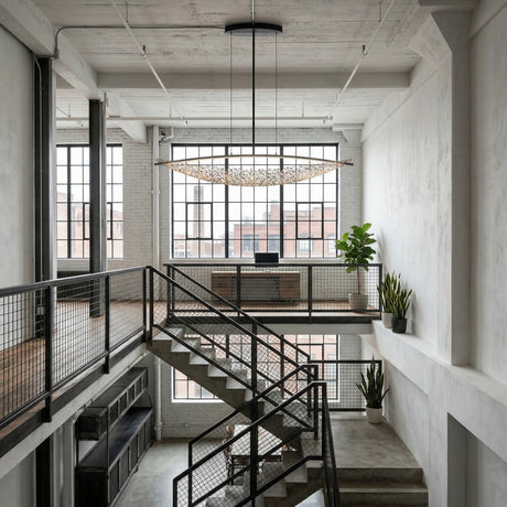 A modern industrial loft with large windows, metal railings, and minimalist decor is filled with natural light and features the sleek Amara LED K9 Crystal Suspension Light - Chrome above the contemporary dining area.