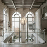 A modern, open interior with large arched windows, a sculptural Mireya 8 Light Metal Chain Veil Chandelier in Nickel, glass railings, exposed concrete, and a sleek staircase overlooking a minimalist courtyard garden.