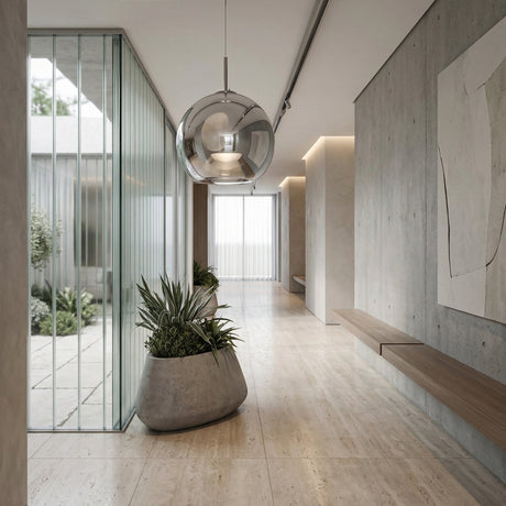 Niori Grand Ball Glass Pendant 40cm in Silver Chrome hanging in a bright minimalist hallway with concrete walls, stone floor, planter and glazed courtyard.