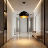 A modern hallway features beige floors, wooden wall panels, a Funk Stout Large Pendant Light in black with gold interior, a minimal wooden bench, a decorative statue in a niche, and glass doors at the corridor’s end.