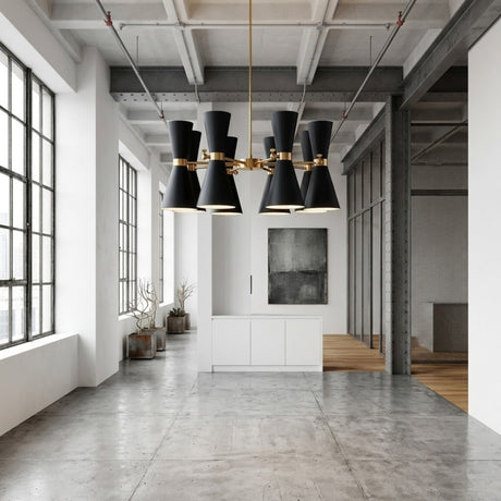 A modern, minimalist loft with large windows, concrete floors, and white walls features the Ramses 8 Light Chandelier - Black hanging from the ceiling, complemented by a small plant and abstract art for decor.