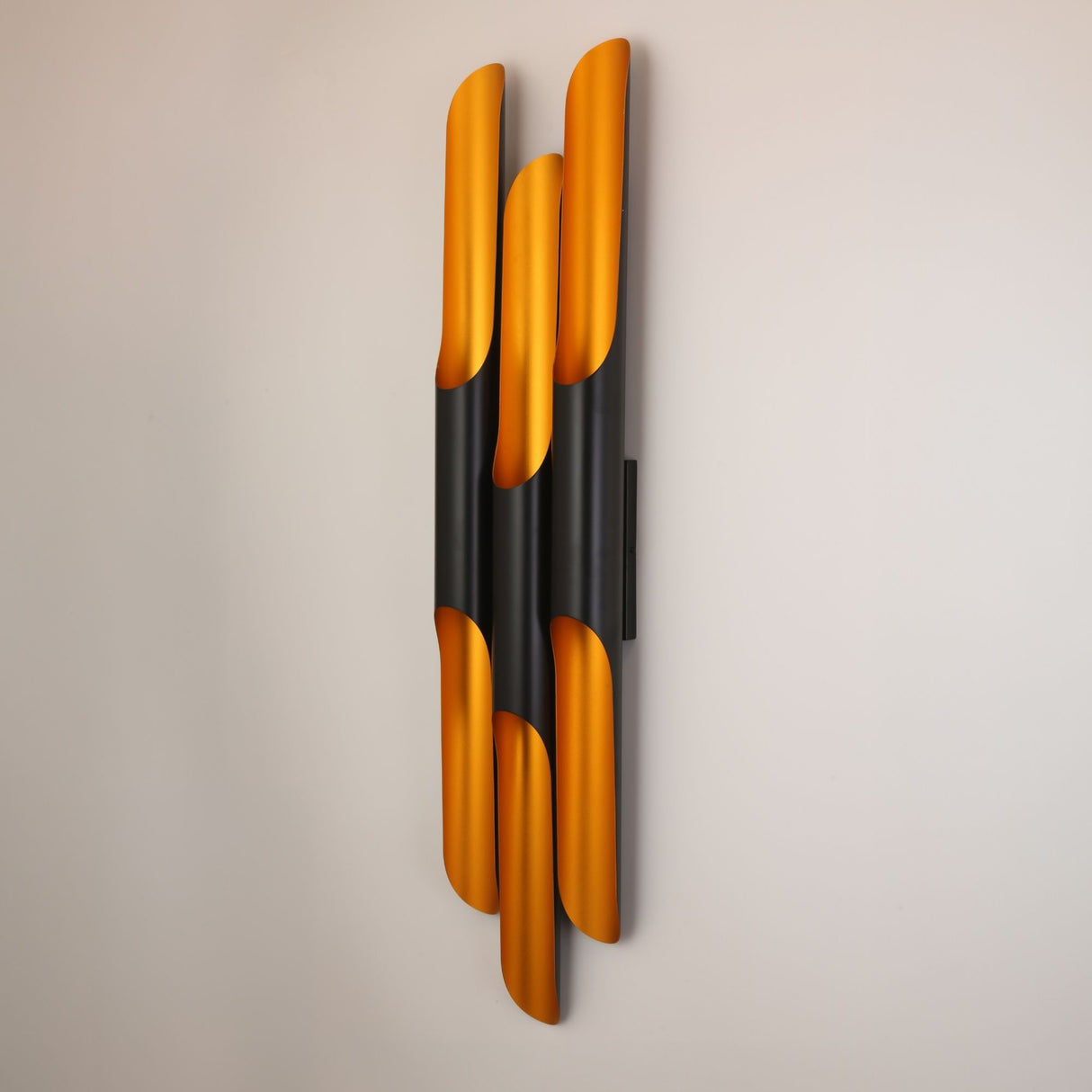 Niori Stealth 6 Light Wall Light in brass and matt black, six staggered vertical tubes with brushed brass interiors mounted on a plain light wall.