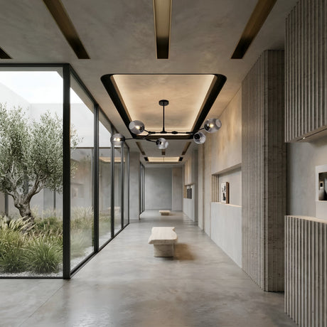 Niori Tree 5 Light Suspension in black with branching arms and smoked glass globes, hanging in a concrete hallway above a stone bench beside a garden window.