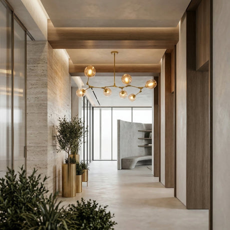 Niori Tree 7 Suspension Light in gold with amber glass globes illuminating a modern hallway with travertine walls, gold planters, and large windows.