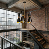 Industrial-style loft with exposed brick walls, large metal-framed windows, and a striking Ramses 5 Light Chandelier - Black. A sleek steel staircase and city skyline enhance the modern, light-filled interior.