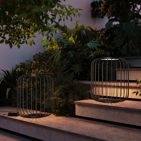 Maytoni Wisp LED bollard lights in graphite steel with vertical cage design, lit on garden steps beside foliage at dusk.