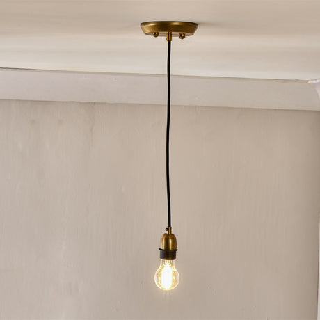 Otti Pendant Light Fitting in antique brass, showing round ceiling rose, black fabric cable, and domed lampholder with exposed bulb against a plain ceiling and wall.