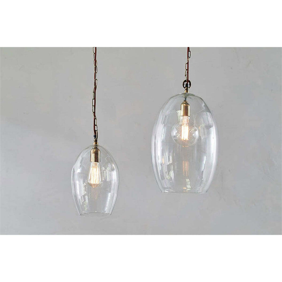 Otoro Small Oval Recycled Glass Pendant Light in clear glass with brass collar and chain, shown beside a larger matching pendant against a plain grey background.