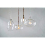 Otoro Small Oval Recycled Glass Pendant Light in clear, tall egg-shaped glass with brass collar and visible lampholder, shown among similar pendants against a plain grey background.