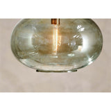 Close-up of the Otoro Large Round Recycled Glass Pendant Light in green, showing the smoky-tinted flattened sphere shade, brass collar fitting, and visible bulb against a plain light background.