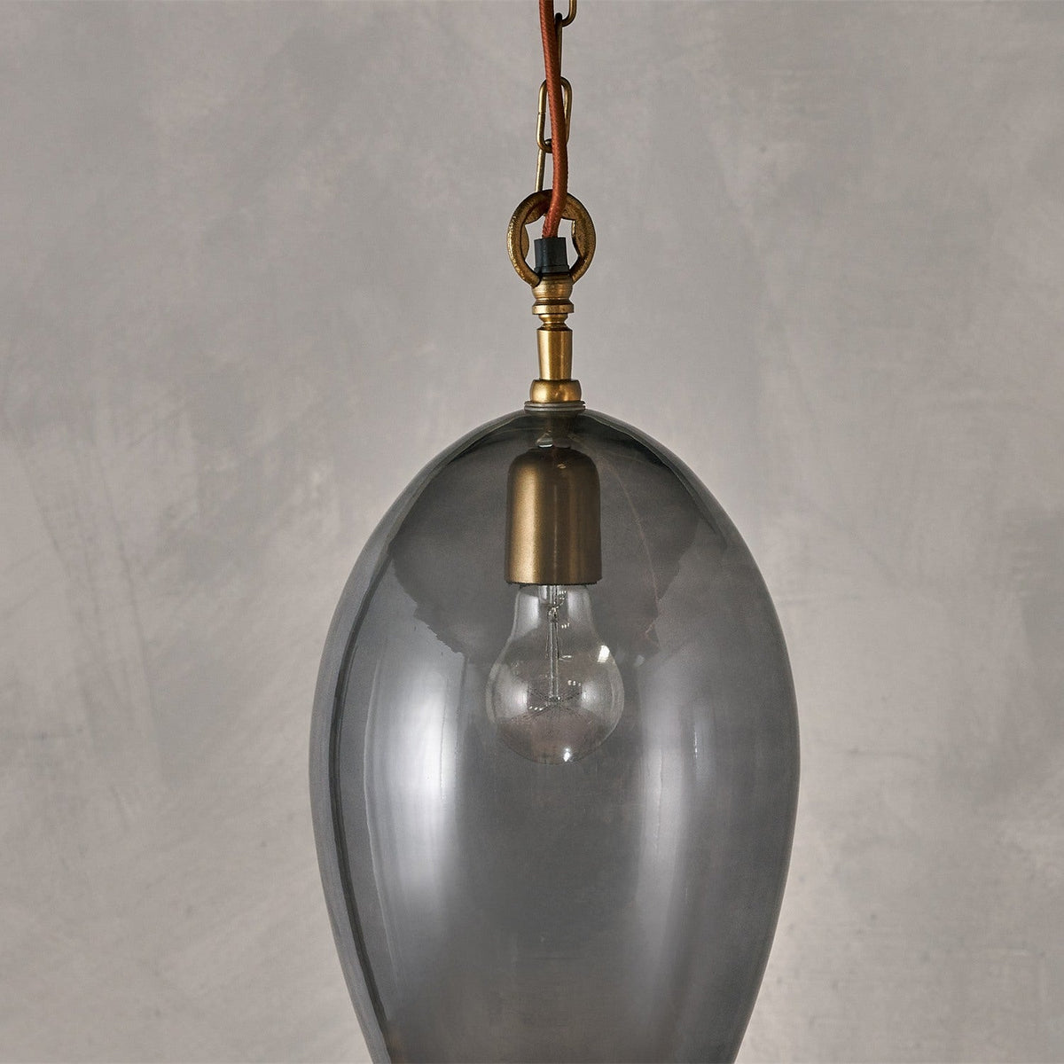 Otoro Small Oval Recycled Glass Pendant Light in smoke, an egg-shaped glass shade with brass collar and chain, exposed bulb visible, shown against a plain grey background.
