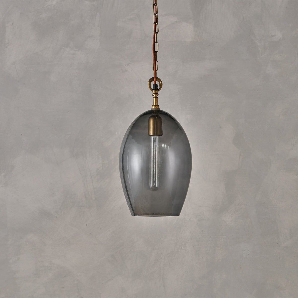 Otoro Large Oval Recycled Glass Pendant Light in smoke, an egg-shaped shade with brass collar and fitting on a rust fabric flex and chain, shown against a plain grey background.
