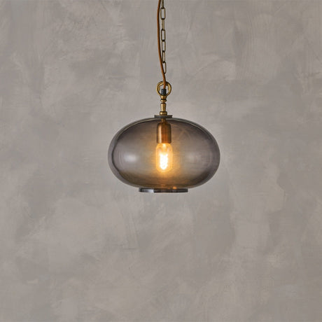 Otoro Small Round Recycled Glass Pendant Light in smoke grey, a flattened sphere shade with brass collar and chain, lit bulb visible, on a plain grey background.