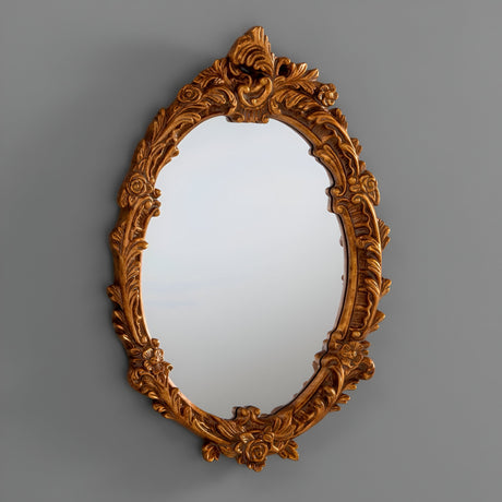The Illuna Oval Wall Mirror in Dark Gold features a vintage-inspired design with an ornate frame, showcasing intricate floral and leaf patterns set against a simple gray backdrop. Its dimensions are 64x46cm.
