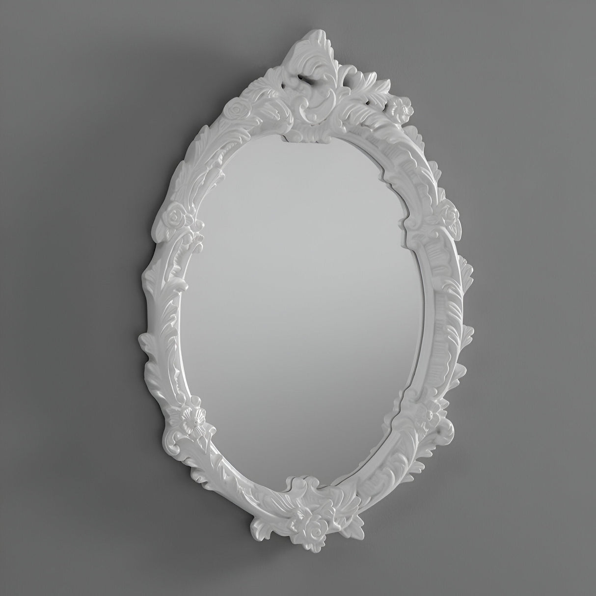 The Illuna Oval Wall Mirror White - 64x46cm, featuring an ornate design with intricate floral and leaf patterns on its white frame, stands out as a striking piece of home decor against a plain gray background.