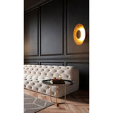 Mantra Orion semi-flush ceiling light illuminated on a dark panelled wall above a tufted cream sofa, showing its gold leaf interior and matt black dome.