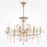The Sevilla 8 Light Chandelier - Gold, lavishly decorated with crystals and eight flame-shaped bulbs, gracefully hangs from a matching gold chain and base against a plain white backdrop.