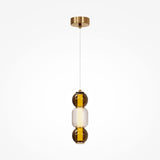 The Drop LED Pendant Light - Gold is a modern pendant featuring a brass ceiling mount and vertical glass fixture with two amber spheres encasing a textured, translucent center. Perfect for modern décor, its white cord offers adjustable lighting to enhance any ambiance.