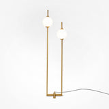 The Sixth Sense 2 Light LED Floor Lamp features two spherical white glass shades at different heights on sleek brass-finished metallic rods, resting on a square base. A black cord complements its design, enhancing ambient lighting against a plain white background.