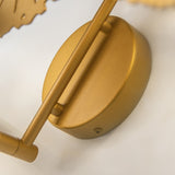 A close-up view of the Lovetann 4 Light Wall Light features a smooth matte brass finish and metallic gold perforated metal discs, mounted on a rod with a rounded base and visible screw. It rests on a light surface.