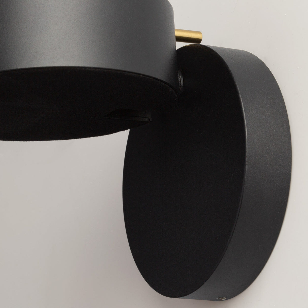 The Nuance LED Movable Head Wall Light showcases a modern cylindrical design in black with gold detailing, mounted on a round base. Its sleek matte finish complements its energy-efficient LED system, enhancing any light-colored wall.