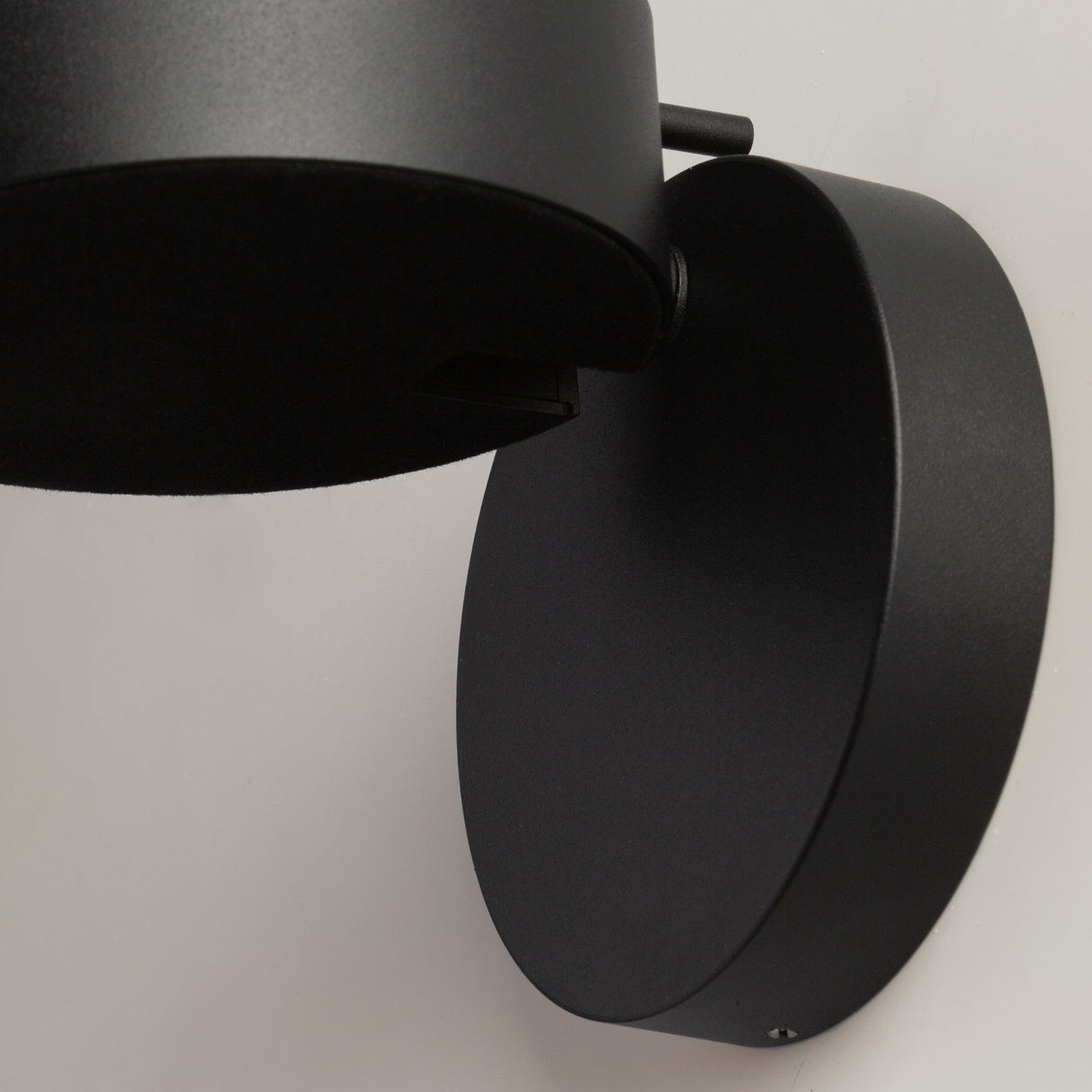 Close-up of the Nuance LED Movable Head Wall Light - Black, showcasing its modern minimalist design. This energy-efficient lighting solution features a lamp on a circular base against a plain white background.