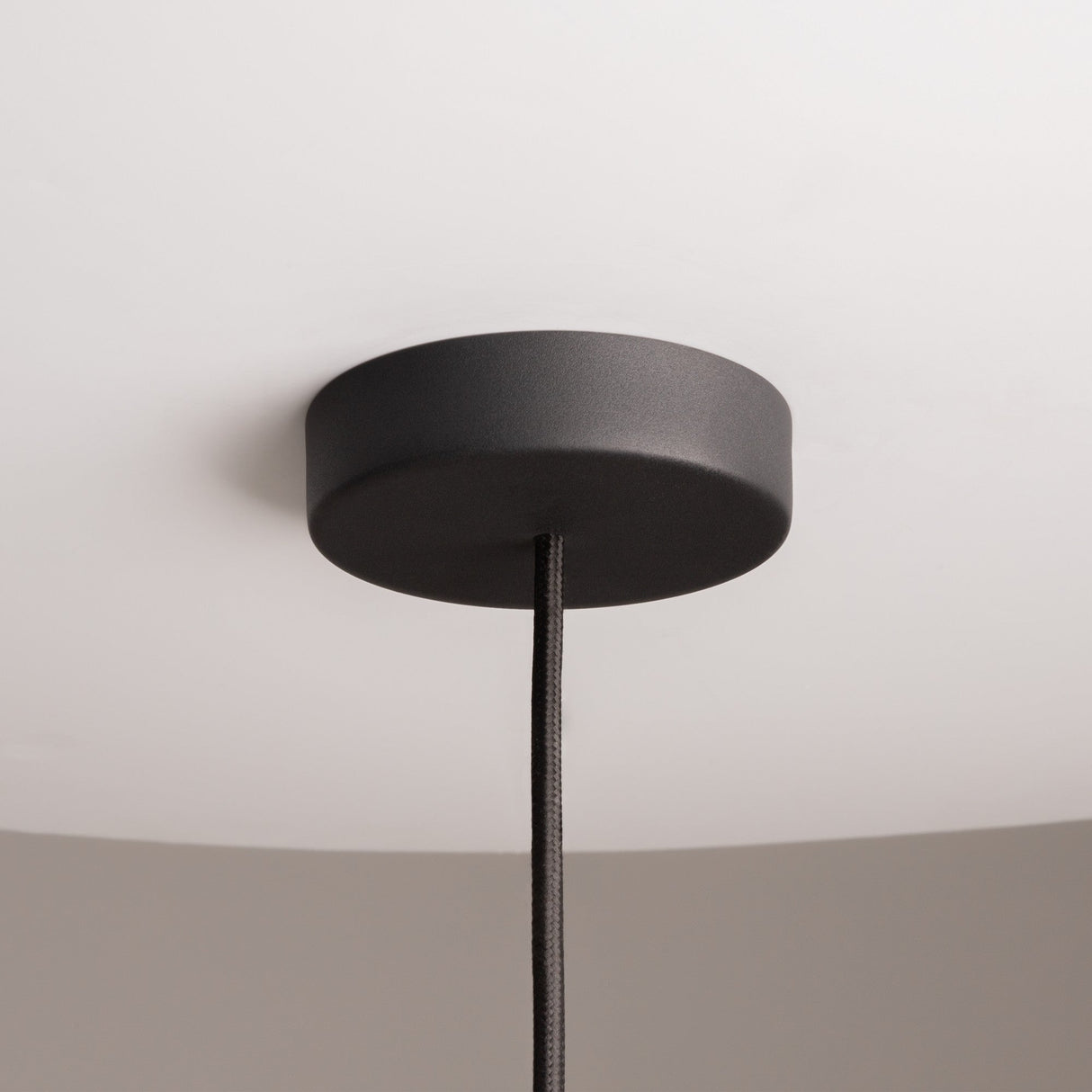 The Cane Pendant Light 30cm in black wicker, featuring a white glass diffuser and adjustable wire, hangs elegantly against a light gray background, adding a modern natural design to any room.