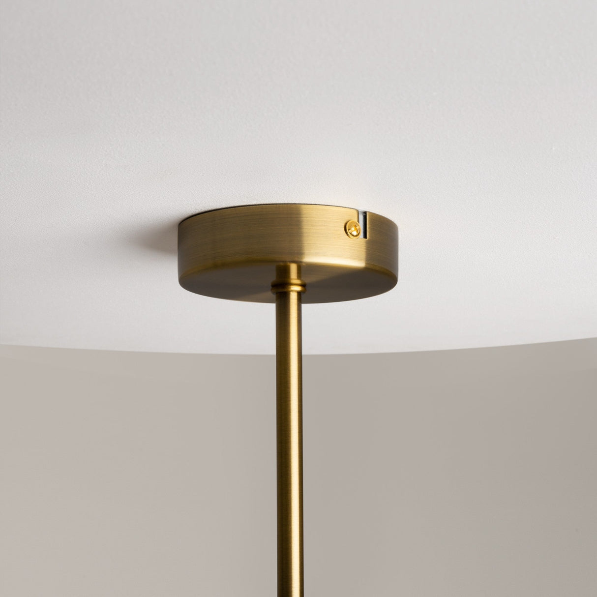 The Miracle 3 Light Pendant, crafted in brass with clear glass shades, descends from a white ceiling via a sleek metal rod. Its minimalistic design exudes contemporary style, enhanced by the warm brass tone against the neutral backdrop.