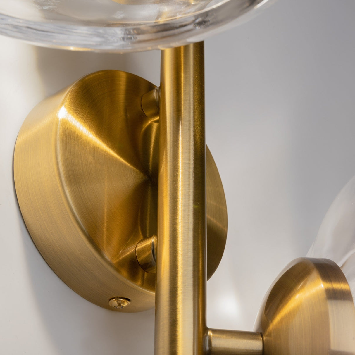 Close-up of the Miracle 2 Light Wall Light, showcasing its Art Deco-inspired brass finish with a sleek brushed texture and featuring a round base with a rod supporting cast glass.