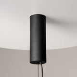 The Cosmo LED Linear Suspension Light, featuring a cylindrical black design with clear glass elements, hangs from a white ceiling with its cord visible at the bottom, offering a futuristic look that contrasts elegantly against the softly lit background.
