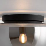 The Glassy Ceiling Flush Light features an exposed bulb within a reflective metallic dome, ideal for compact spaces. It casts a warm glow through smoky black glass and is mounted on a white ceiling.